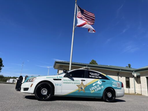 A Walton County Sheriff's Office crime prevention themed vehicle parked in front of a flag pole with the American flag and the state of Florida flag